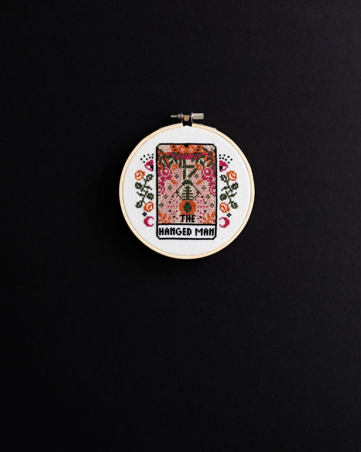 The hanged man tarot cross stitch design on a black background