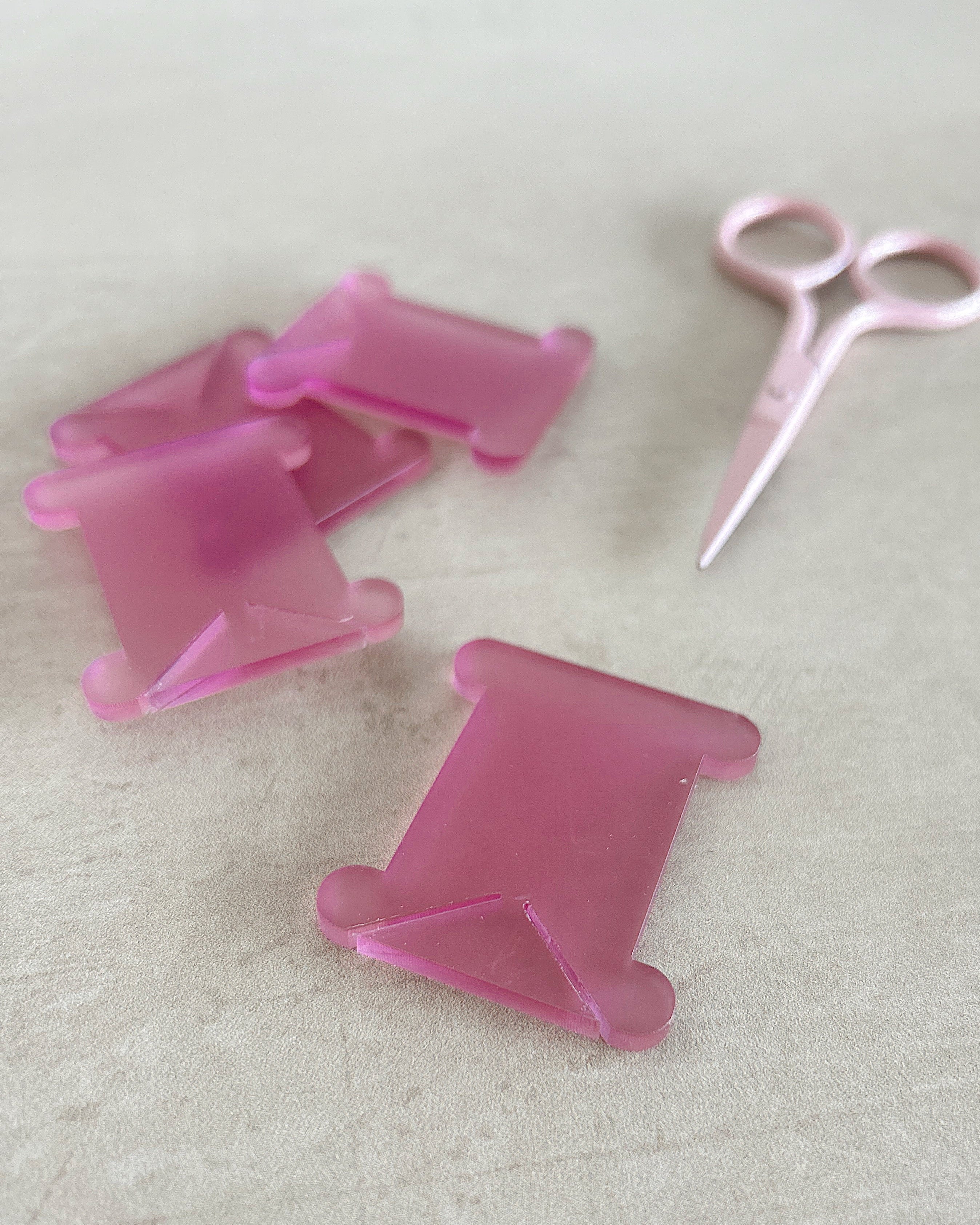 Pink acrylic thread bobbins and a pair of pink scissors on a light background
